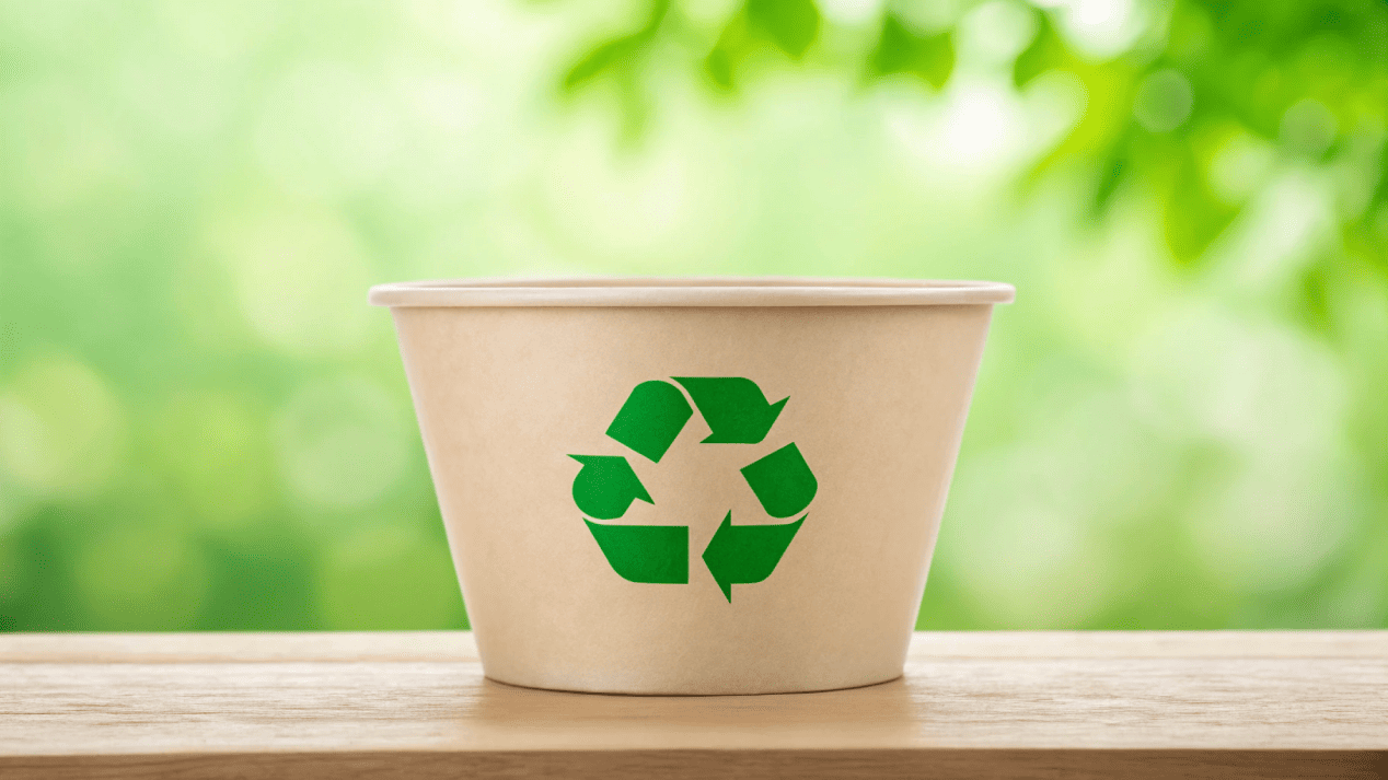 A compostable PLA-lined noodle bowl with a green recycling symbol on it