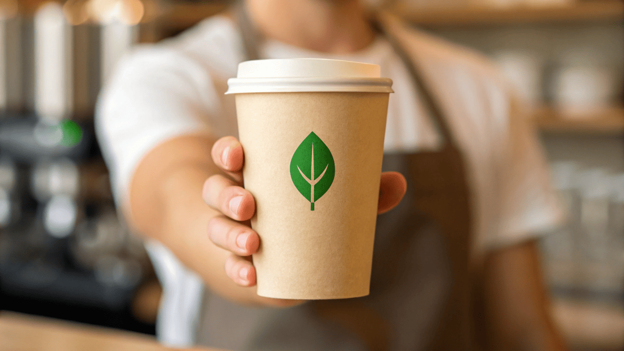 A customer being handed a compostable PLA-lined paper cup with a green leaf logo on it.