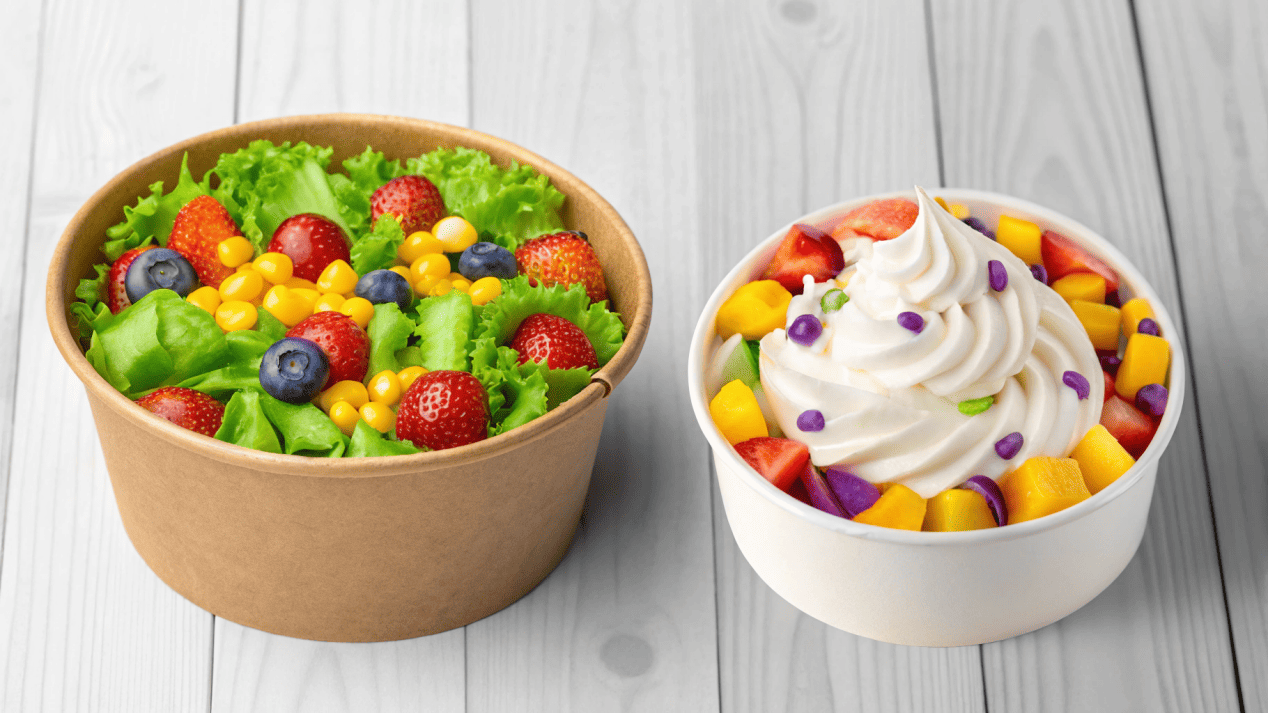 A healthy salad in a Kraft bowl next to colorful froyo in a white bowl.