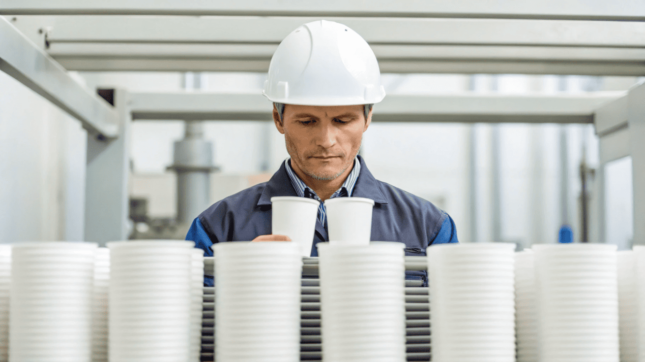 A quality control inspector checking paper cups on a production line