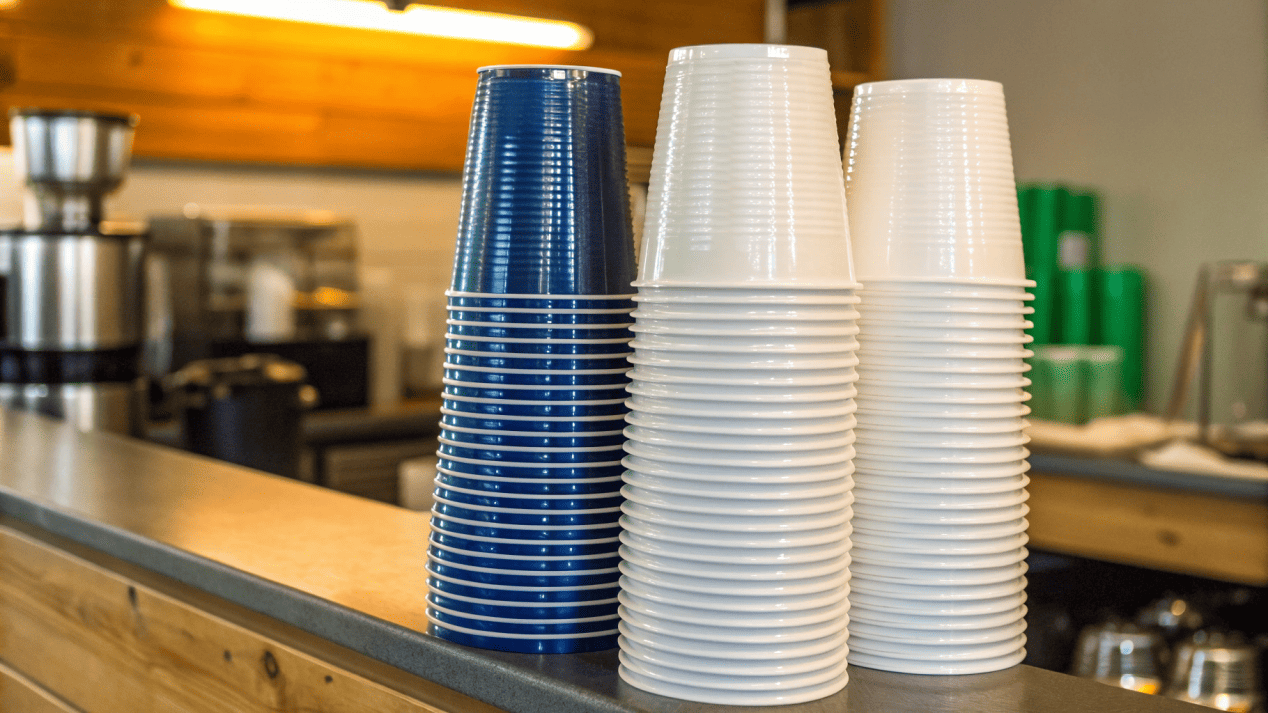 Cost Comparison of Plastic and Paper Cups A stack of plastic cups next to a stack of paper cups with price tags on them.