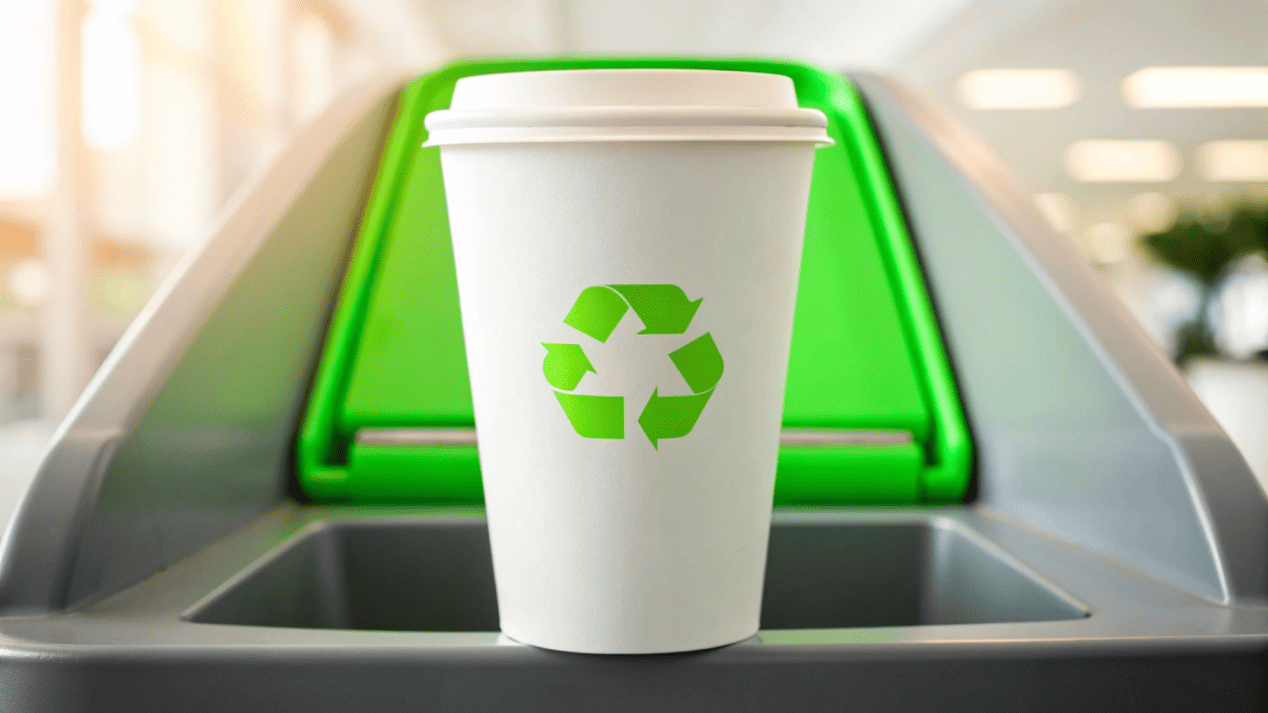 Truly Recyclable Water-Based Coated Cup A new water-based coated cup going into a recycling bin with a green circular arrow symbol.