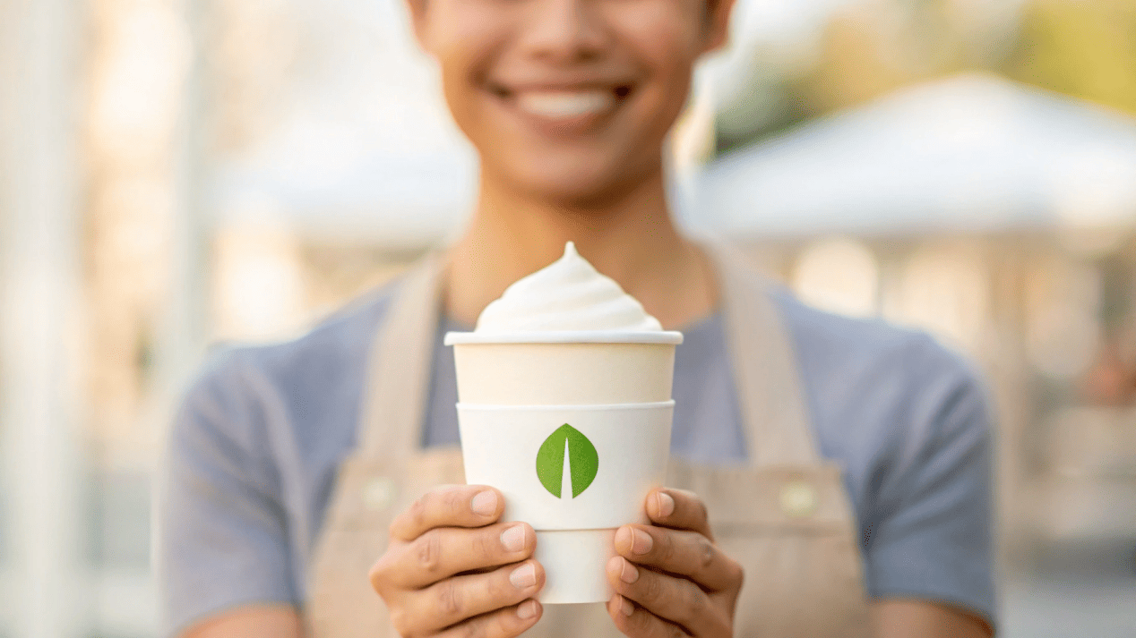 A customer smiling, holding a premium ice cream cup that clearly displays eco-friendly branding.